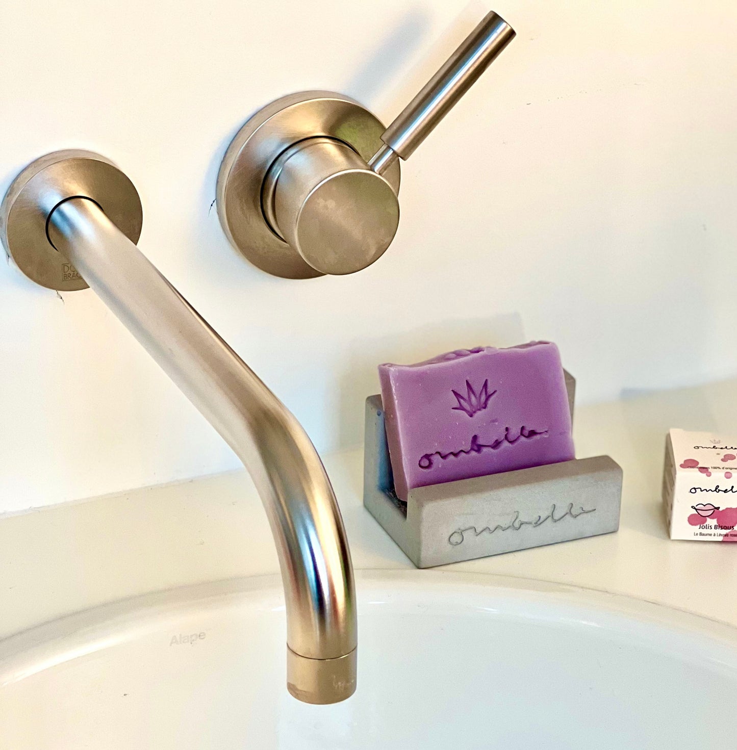 Vegane Naturseife in eleganter Design-Seifenhalter mit Design-Armatur. Im HIntergrund sieht man eine Lippenpflege der Marke Ombelle.