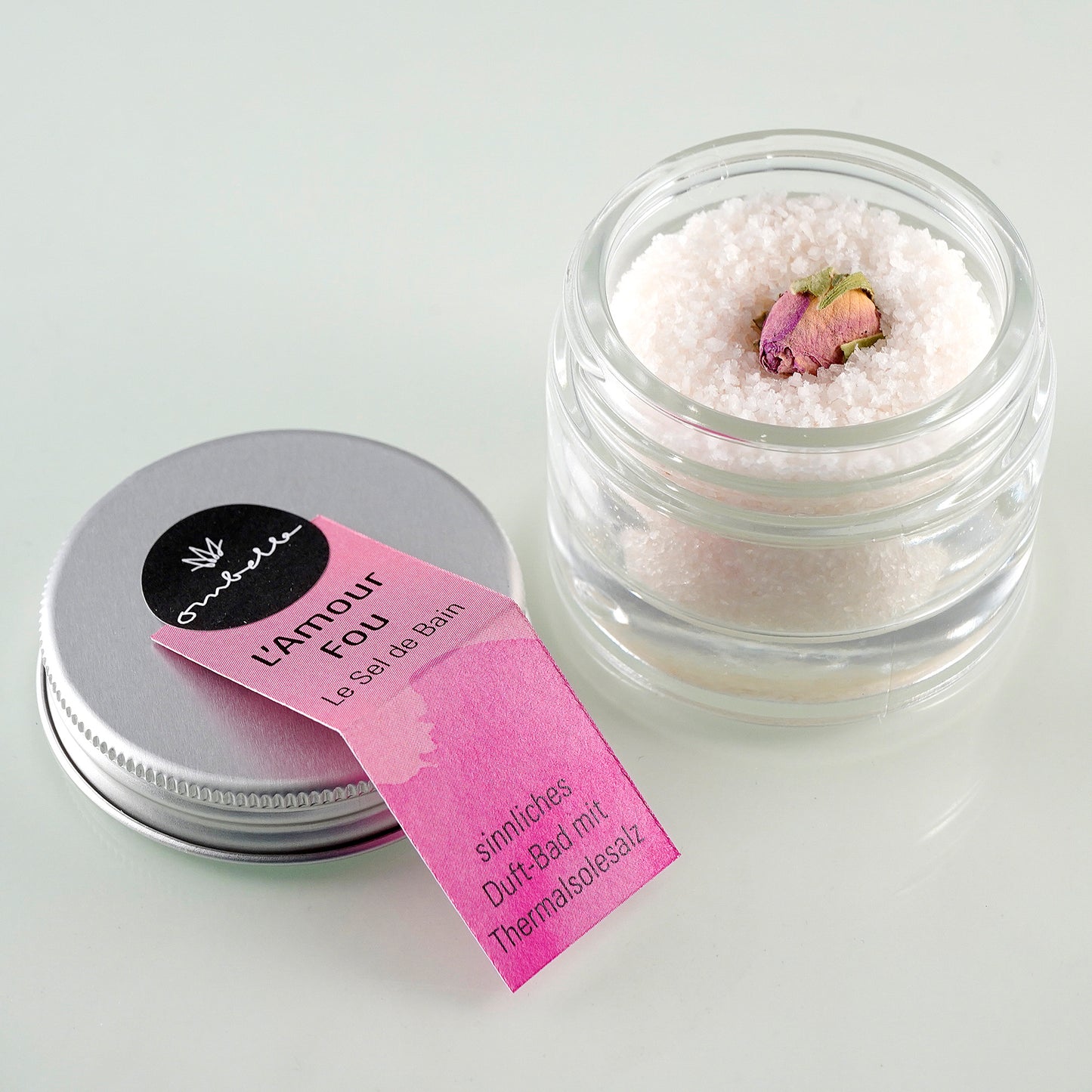 Ombelle Thermalsalz L'Amour Fou 30g im Glastiegel mit geöffnetem Deckel. in das Salz eingebettet, findest du eine echte Rosenblüte.